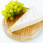 Brie cheese on wooden round board with bunch of white grapes