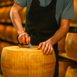 Closeup of a man slicing a Parmigiano Reggiano cheese wheel