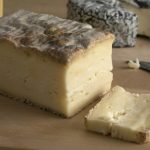 Piece of Italian Taleggio and a slice on a cutting board close up